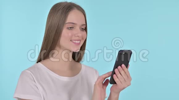 美丽的年轻女性使用智能手机蓝色背景视频的预览图