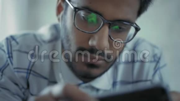 特写镜头戴眼镜的印度男人用智能手机听音乐视频的预览图