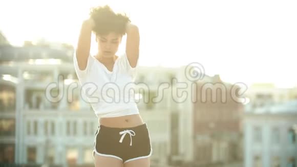 一位年轻女子穿着高跟鞋表演迷人的舞蹈在屋顶上玩她的卷发日落视频的预览图