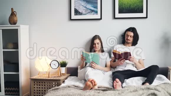 美丽的一对夫妇坐在床上一起享受爱好视频的预览图