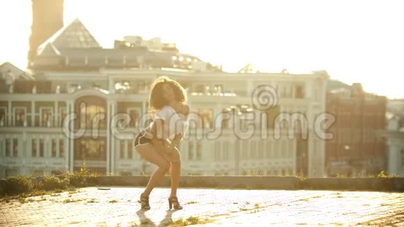 一个穿着小短裤的年轻女子站在地上在屋顶上表演迷人的性感舞蹈明亮的视频的预览图