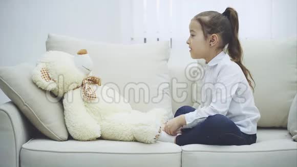 可爱的小女孩坐在沙发上和她的泰迪说话把她的手指轻轻地弯曲视频的预览图
