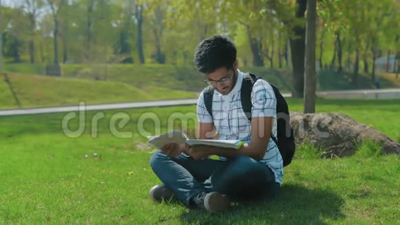 戴眼镜的印度学生背包在城市公园的草坪上研究抽象物视频的预览图