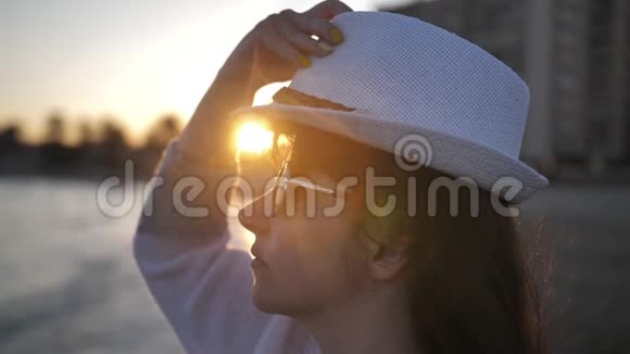 太阳眼镜的女人在日落时戴着帽子靠近大海慢动作视频的预览图