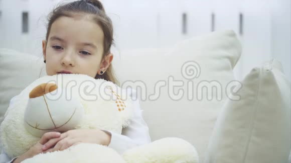 小迷人的女孩心烦意乱她坐在沙发上拥抱她的大毛绒朋友视频的预览图