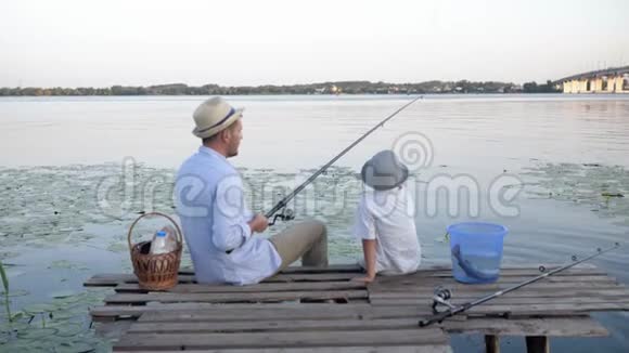 孩子们钓鱼快乐的男渔夫教他的小儿子如何在河里钓鱼而坐在鱼竿上视频的预览图