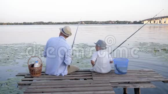 无忧无虑的童年幸福的家庭小男孩和男人懒洋洋地坐在河边的码头上钓鱼视频的预览图