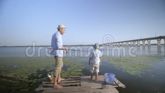 钓鱼渔夫父亲在家中教他的小儿子在河边码头钓鱼视频的预览图