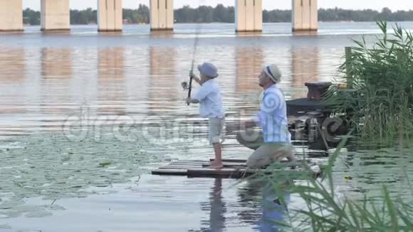 家庭爱好男渔夫教小男孩在芦苇丛中坐在木筏上钓鱼视频的预览图