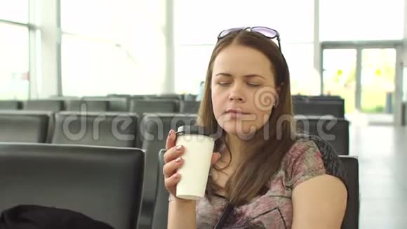 年轻疲惫的女人在机场候机室喝咖啡特写镜头视频的预览图