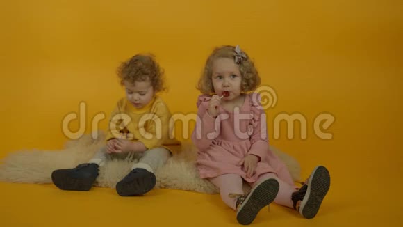 两个卷曲的孩子坐在地毯上吃棒棒糖视频的预览图