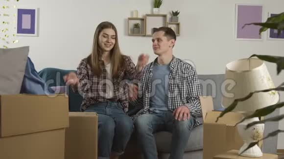 微笑的情侣拥抱在沙发上看着纸板箱视频的预览图