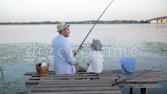 有爱心的父亲有爱心的父母和他的孩子在一起聊天坐在河边的码头上钓鱼视频的预览图