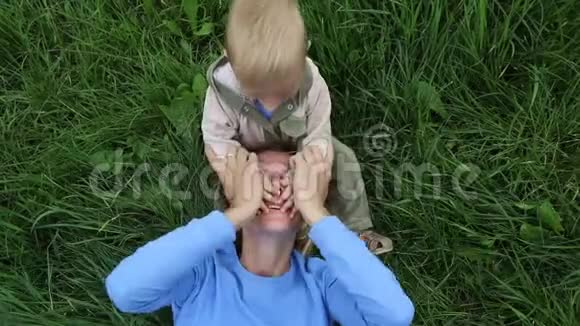 母亲躺在草地上坐在儿子身边和他一起笑孩子闭上双手看妈妈玩捉迷藏视频的预览图