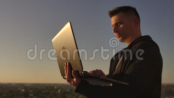 程序员一个黑客在屋顶上带着一台笔记本电脑在日落时说键盘上的错误代码然后看城市景色视频的预览图
