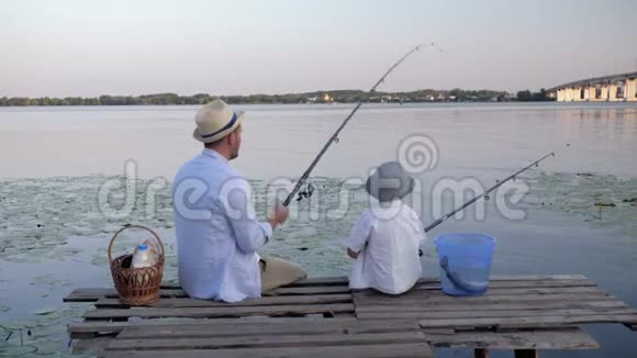 快乐的父母体贴的父亲和他心爱的儿子在河边的码头钓鱼在家中的周末在芦苇丛中钓鱼视频的预览图