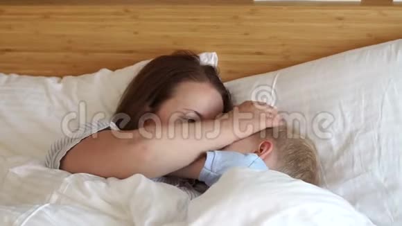 睡意朦胧的妈妈和儿子躺在卧室的床上的白色枕头上视频的预览图