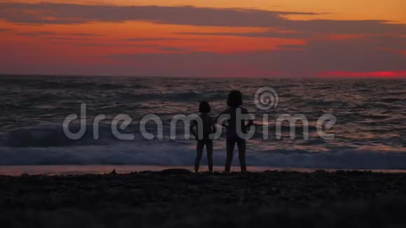 日落时两个小女孩站在大海或海洋边视频的预览图