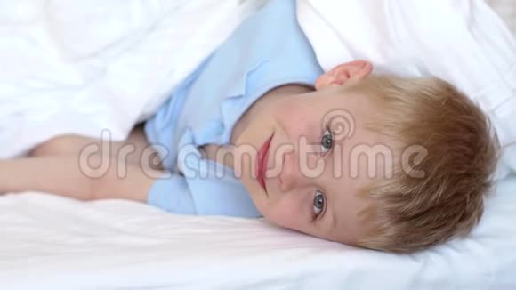 特写一个小蓝眼睛男孩的脸在一张白色毯子下的床上视频的预览图