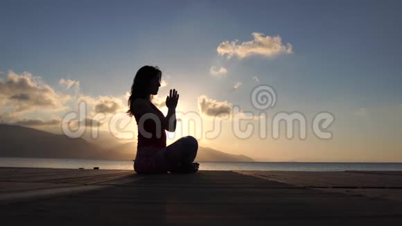 一个年轻漂亮的女人在日出时在海边慢动作地冥想视频的预览图