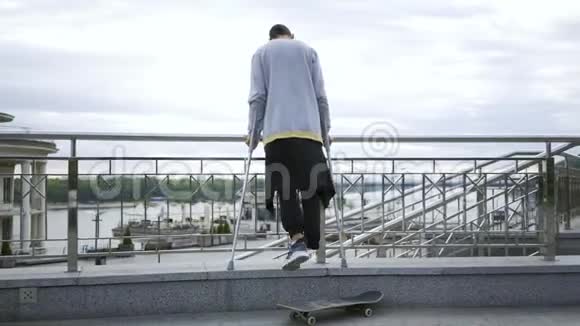 后景男子单腿站在拐杖上的街道与滑板残疾人的积极生活这就是视频的预览图