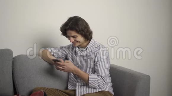 客厅里坐在沙发上用智能手机的微笑男人视频的预览图
