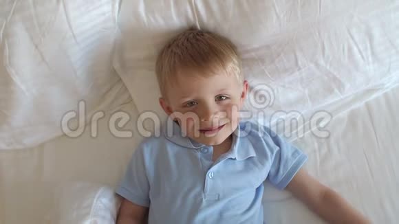 在床上用条纹毯子或被子盖住他的脸的小男孩的俯视图视频的预览图