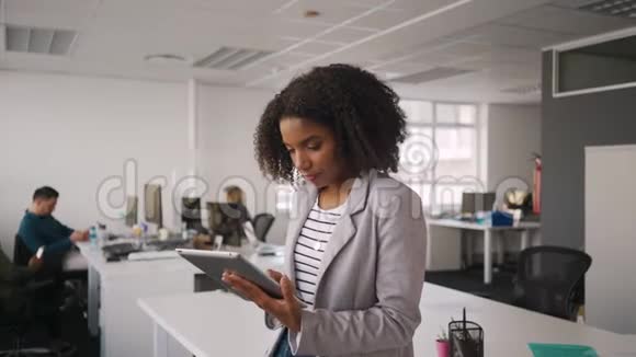 快乐年轻的职业女商人在办公室里使用数字平板电脑的肖像和在后台工作的同事视频的预览图