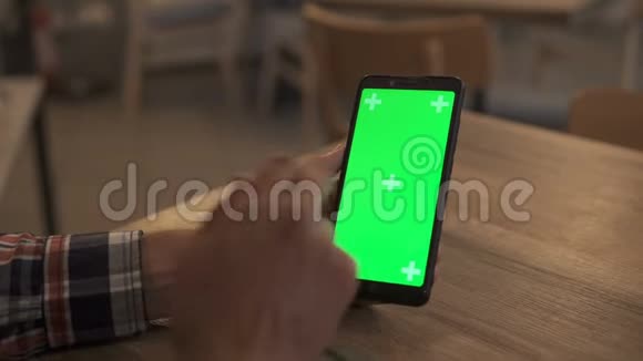 一名男子手持绿色模拟屏幕智能手机的特写镜头使用应用程序现代手机在背景中舒适视频的预览图