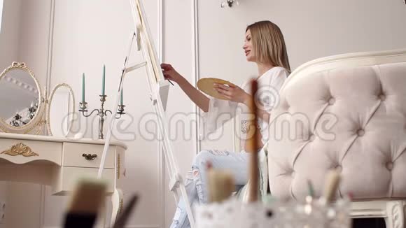 一个怀孕的女孩画了一幅画坐在明亮卧室的床上视频的预览图