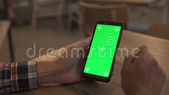 一名男子手持绿色模拟屏幕智能手机的特写镜头使用应用程序现代手机在背景中舒适视频的预览图