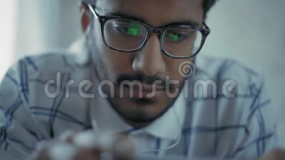 特写镜头戴眼镜的印度男人正在你的智能手机上观看带有耳机的视频视频的预览图