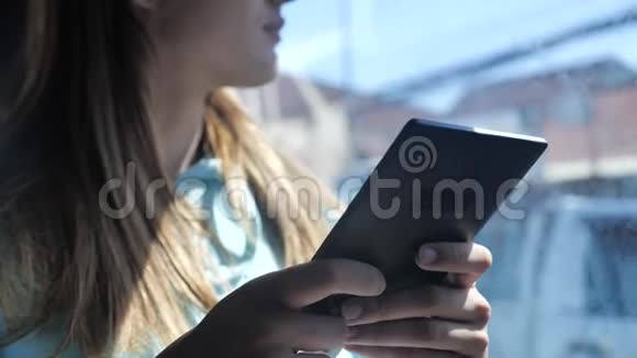 一个年轻的女人正在公共汽车上读一本电子书在窗外阳光明媚的一天背景上的棕榈树4k视频的预览图