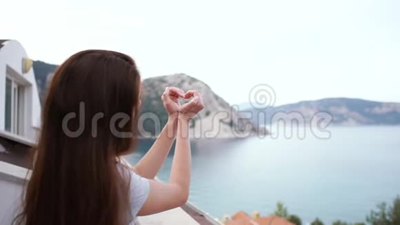 一个女孩用手做了一个心形图案慢悠悠地站在阳台上视频的预览图