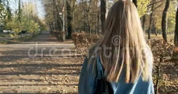 年轻快乐的女孩走在秋天的公园里年轻迷人的女人在阳光下散步和微笑背面视频的预览图