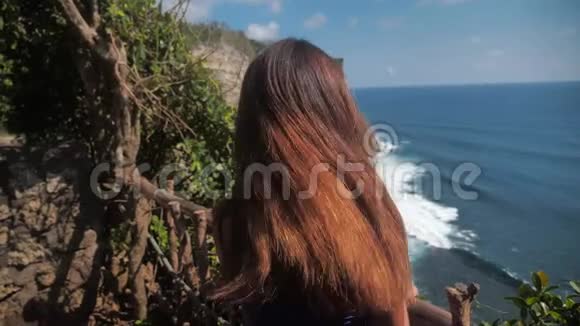 特写肖像一位年轻女子带着棕色头发微笑风吹看着海洋穿绿松石的女孩视频的预览图