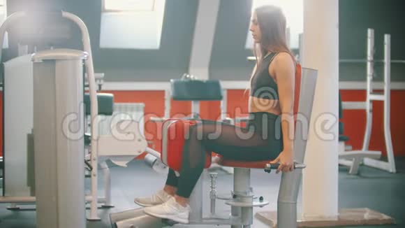 一名运动员女子在健身房训练用蝴蝶训练装置进行腿部练习视频的预览图