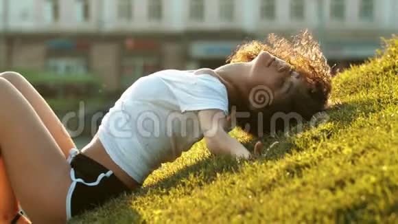 迷人的瘦小女人卷发从草地上站起来看着镜头视频的预览图