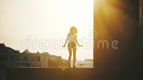 一位留着卷发和小短裤的年轻女子在建筑物的背景下表演迷人的脱衣舞视频的预览图