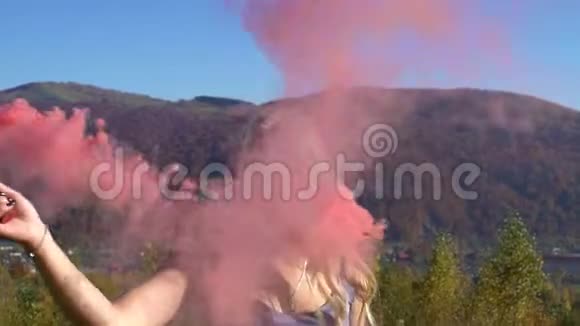年轻迷人的情感女孩带着彩色烟雾在山里跳舞视频的预览图