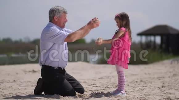 在海滩上孙女和祖父把沙子筛到对方手4K慢慢视频的预览图