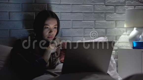 女孩咳嗽剧烈感冒失眠晚上在笔记本上看电影视频的预览图