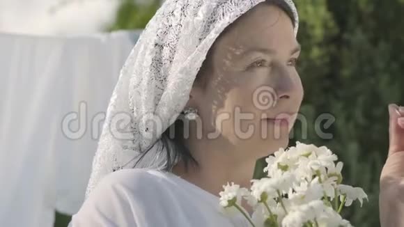 可爱的成熟女人头上戴着白色披肩在户外的晾衣绳上撕下雏菊花瓣华盛顿积极正面视频的预览图