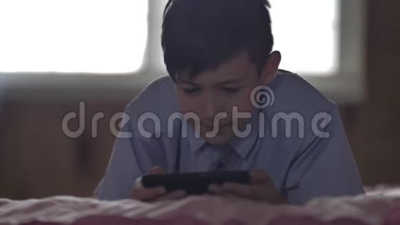 男孩躺在家里的床上用手机玩游戏视频的预览图
