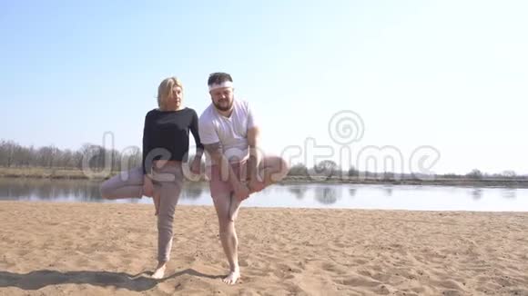 一位白种人的男教师和一位女教师在自然界的河岸上从事动态瑜伽冥想技巧视频的预览图