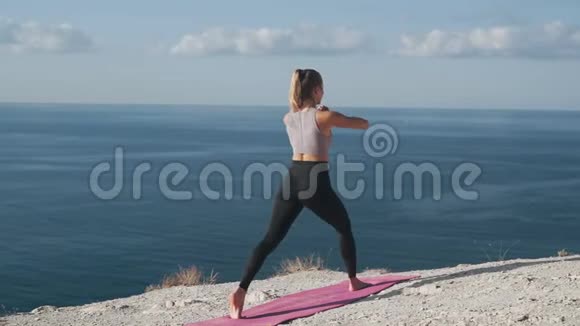 女人蹲在户外的垫子里训练她的身体有海景有背面风景视频的预览图