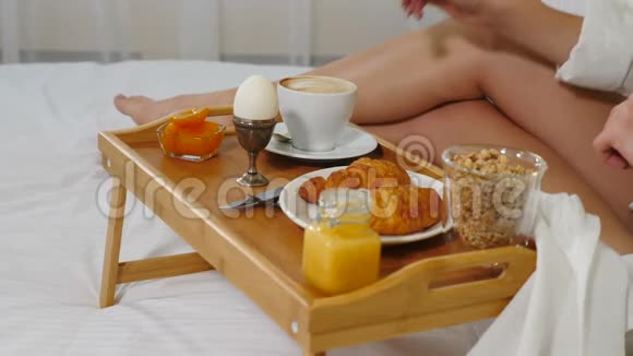 早上在舒适的酒店房间喝咖啡的年轻女人的特写镜头带鸡蛋的白色床上用品桌上托盘视频的预览图