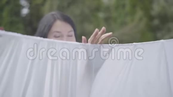 肖像可爱成熟的女人长发白色的衣服挂在晾衣绳上看着户外的相机洗衣日视频的预览图