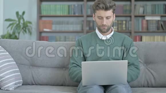 严肃的年轻人坐在沙发上用笔记本电脑工作视频的预览图