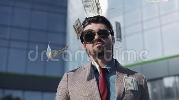 一个穿着现代西装戴着墨镜的富人站在办公楼附近的大街上一堆堆钱掉了下来视频的预览图